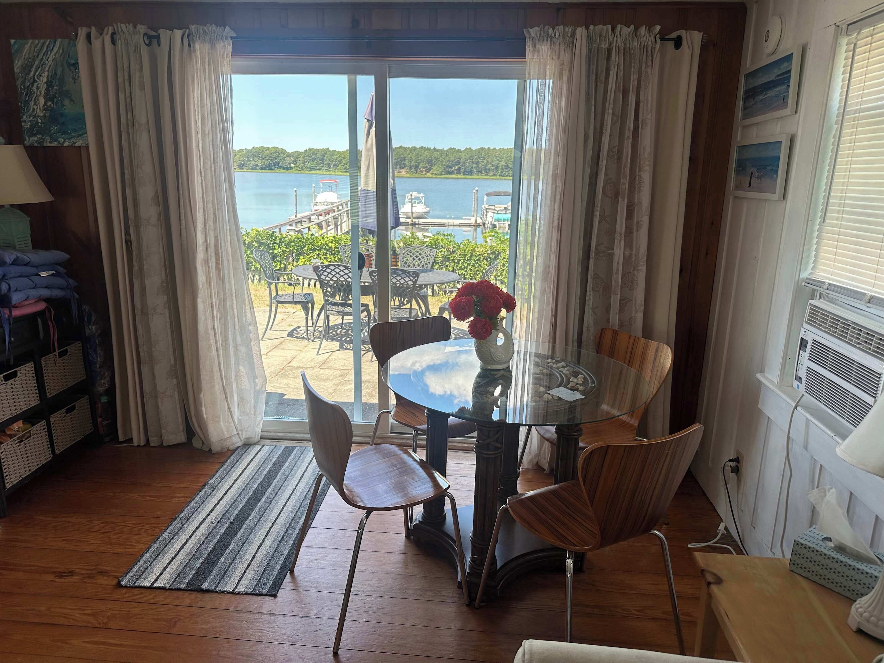 Una habitación con una mesa de vidrio, sillas, vista al mar y suelo de madera.