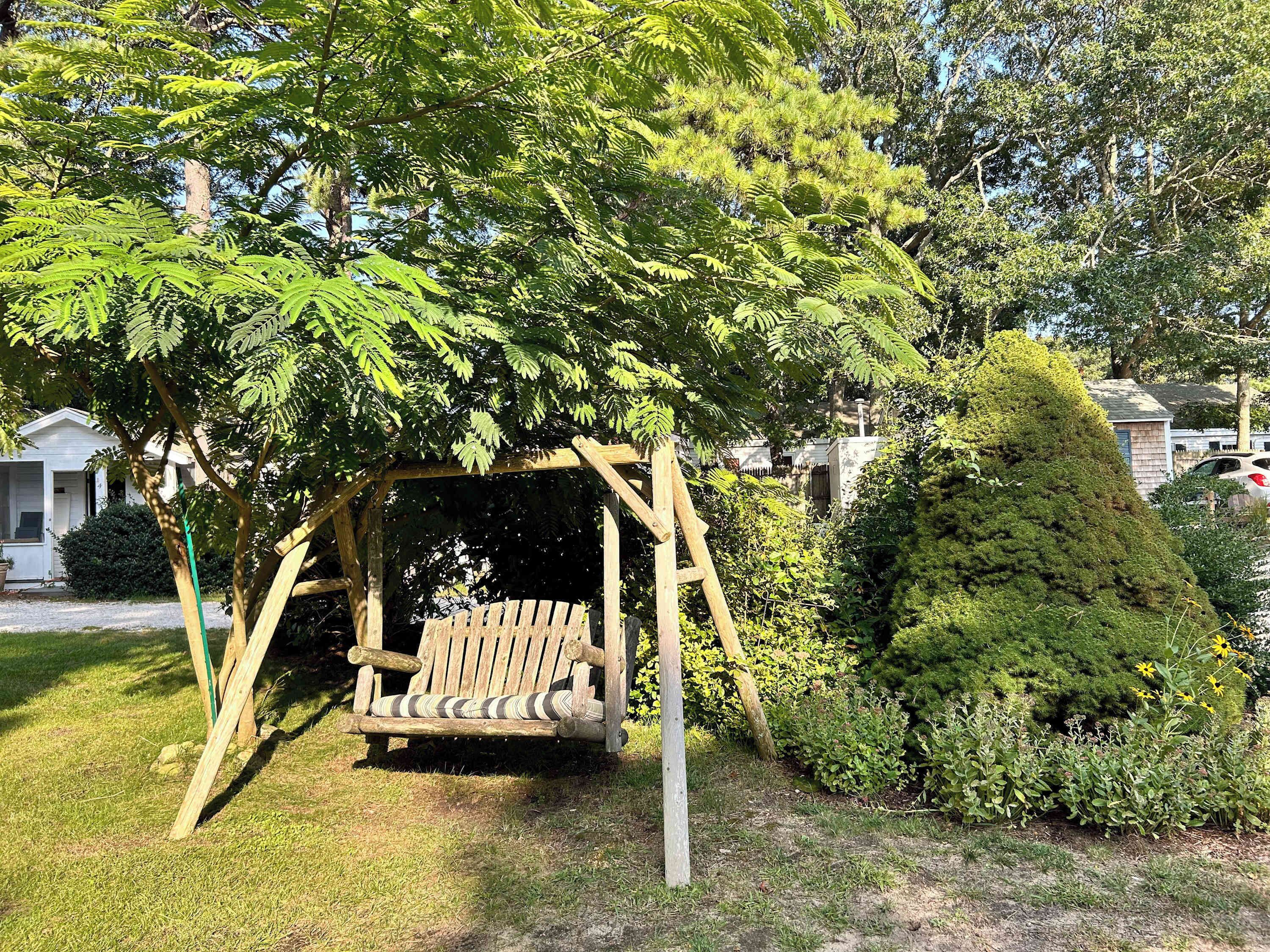 A wooden swing set under a tree in a residential area.