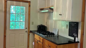 Une cuisine compacte équipée d’une cuisinière, de meubles en bois et d’une fenêtre donnant sur un espace verdoyant.