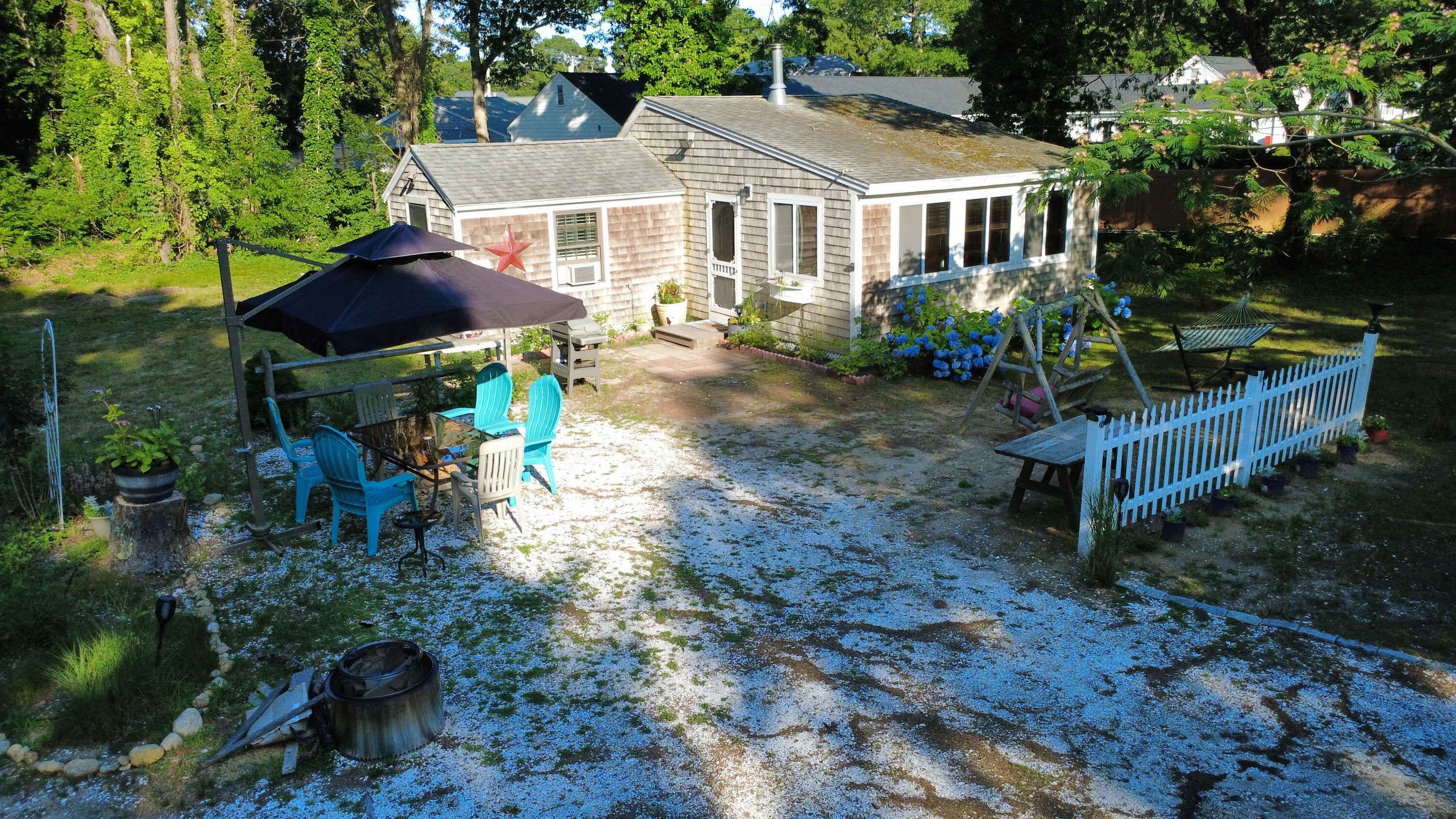Een huis met een patio, een schommel en een omheinde tuin.