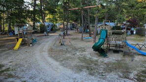 Ein Spielplatz mit Rutschen und Schaukeln, umgeben von Bäumen und Häusern.