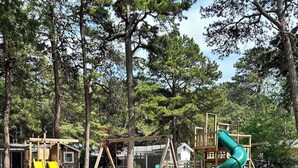 A playground with swings and a slide, surrounded by trees.