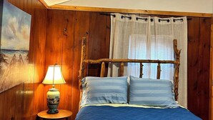 A bedroom with a wooden headboard, a bed with blue bedding, a lamp on a side table, and a painting on the wall.
