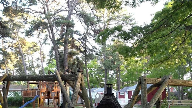 A rustic outdoor area with a wooden play structure, a small black chimney, and potted plants.