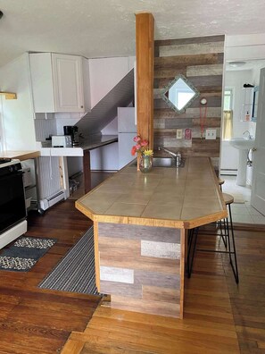 A modern kitchen with a central island, white cabinets, a wooden accent column, and a stone backsplash. - Spacious 4 Bedroom House on Campground/Retreat! (Yarmouth)