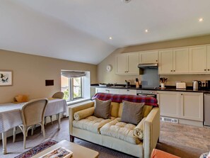 A cozy living room with a sofa, a dining table with chairs, a kitchen area with cabinets and appliances, and a window with a view.