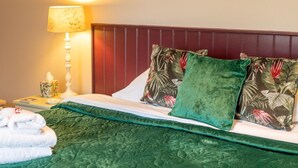 Un letto rifatto con cura, con una coperta verde, due cuscini a motivo tropicale, una lampada da comodino e un pacchetto di fazzoletti sul tavolino.