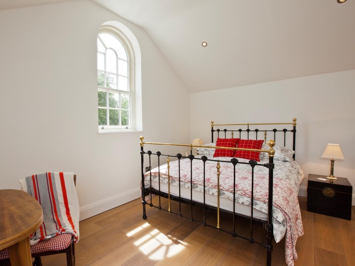 Ein Schlafzimmer mit Bett, Fenster, Sessel, Tisch und Nachttisch.