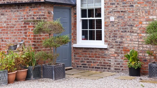 A brick building with a white window, a door, and potted plants. - 1 Bed in York (oc-g0043) (Holtby)