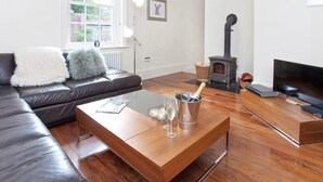 A modern living room with a leather sofa, a wooden coffee table with a bottle of champagne and glasses, a fireplace, and a television. - 1 Bed in York (oc-g0043) (Holtby)
