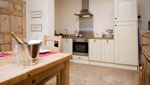 A kitchen with white cabinets, a stainless steel range hood, a dining table with a bottle of champagne, and a wooden chair. - 1 Bed in York (oc-g0043) (Holtby)
