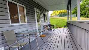 Een overdekt terras met een tafel, stoelen, een hangmat en uitzicht op een gazon.