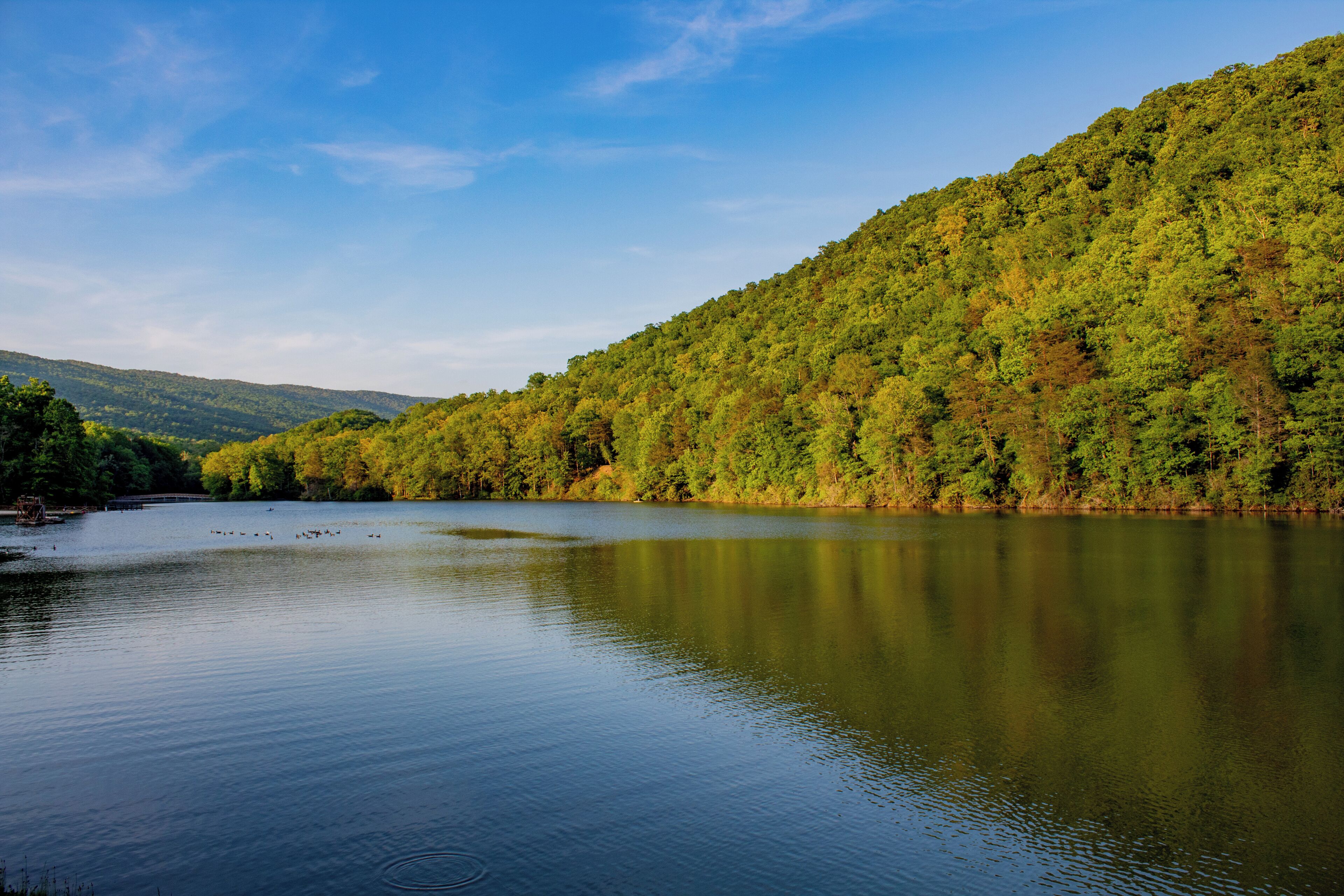 A calm lake surrounded by forested hills.