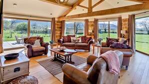 Ein großzügiges Wohnzimmer mit Ledersofas, einem Holztisch und großen Fenstern mit Blick ins Grüne.