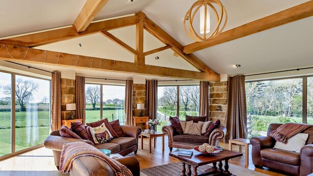 Ein geräumiges Wohnzimmer mit Ledersofas, einem Holztisch und großen Fenstern mit Blick ins Freie.
