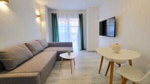 Un saló modern amb un sofà, una taula rodona petita i un televisor fixat a la paret.