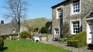 A stone building with a grassy yard, a white dog, and a bench. - 4 Bed in Kettlewell (oc-g0041) (Starbotton)