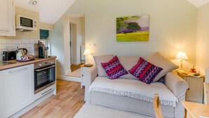 A cozy kitchen with a microwave, toaster, and oven, a sofa with patterned cushions, and a painting on the wall. - 1 Bed in York (oc-g0032) (Crayke)