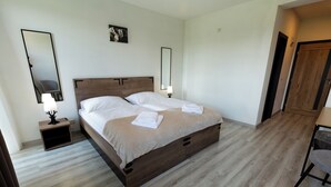 A hotel room with a wooden bed, bedside tables, a chair, and a door. - Penzion Kamence (Trstene)