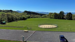 A circular gravel area with a fence, surrounded by a green field and trees, with mountains in the background. - Penzion Kamence (Trstene)