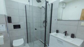 A modern bathroom with a glass-enclosed shower, a white toilet, and a sink with a mirror above it. - Penzion Kamence (Trstene)
