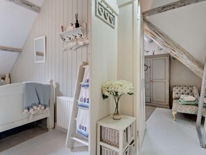 Ein Schlafzimmer mit schrägen Wänden, einem Heizkörper, einem weißen Schminktisch, einem Stuhl, einem kleinen Tisch mit einer Vase und einem Regal mit Haken.