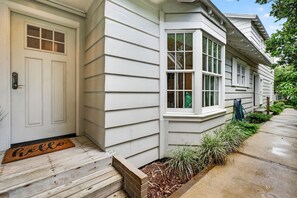 Une maison avec une porte d’entrée, un paillasson, un petit jardin devant et un chemin menant à la maison.