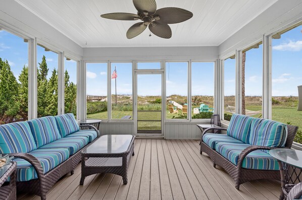 A covered outdoor deck with two wicker sofas, a glass-top table, and a ceiling fan. - Baba's Beach House - Oceanfront Family Cottage (Jacksonville Beach)