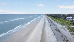 A beach with a long stretch of sand, a clear sky, and houses in the background. - Baba's Beach House - Oceanfront Family Cottage (Jacksonville Beach)