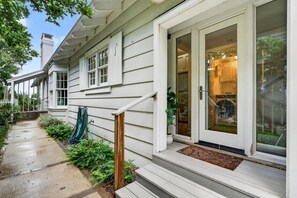 A house with a front porch, a door with glass panels, and a visible kitchen area through the glass. - Baba's Beach House - Oceanfront Family Cottage (Jacksonville Beach)