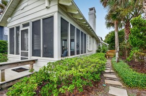 A house with large windows, a wooden deck, and a stone pathway leading to a gate. - Baba's Beach House - Oceanfront Family Cottage (Jacksonville Beach)