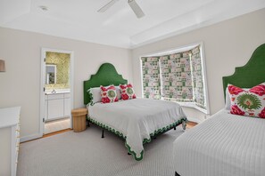 A bedroom with a bed, a window with patterned curtains, a bedside table, and a mirror. - Baba's Beach House - Oceanfront Family Cottage (Jacksonville Beach)