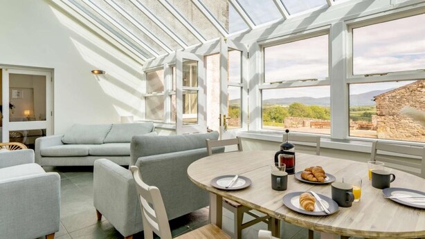A modern interior with a dining area, a sofa, and a view through large windows. - 8 Bed in Cockermouth (oc-82453) (Blindcrake)