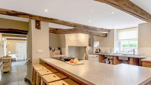 A spacious kitchen with a large island, wooden stools, a brick backsplash, and exposed wooden beams. - 8 Bed in Cockermouth (oc-82453) (Blindcrake)