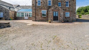 A stone building with a central entrance, multiple windows, and a gravel driveway. - 8 Bed in Cockermouth (oc-82453) (Blindcrake)