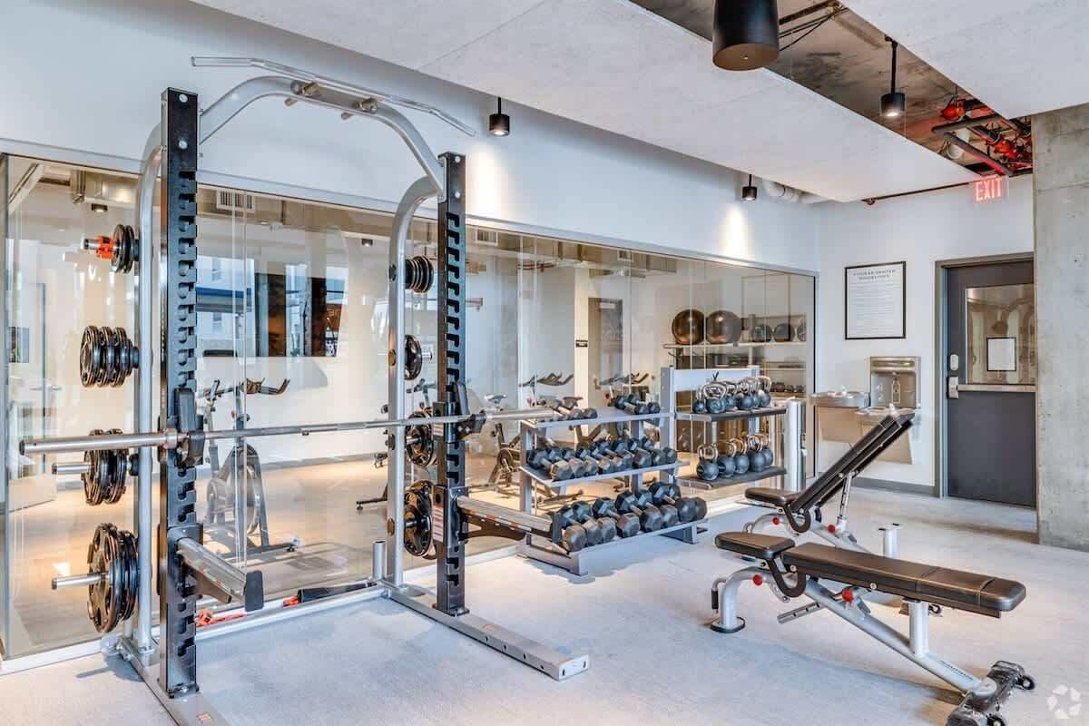 A modern gym with weightlifting equipment, benches, and a mirrored wall.