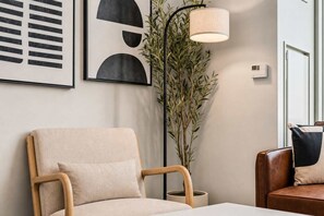 A room with a beige armchair, a floor lamp, a potted plant, and a framed abstract artwork on the wall. - Boulevard Stays Downtown - Studio Rooftop Pool, Gym & Parking 02 (Phoenix)