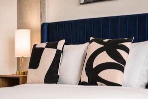 A bed with a blue upholstered headboard, white bedding, and three patterned pillows. - Boulevard Stays Skyline Studio Rooftop Pool, Gym & Parking (Phoenix)