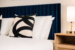 Ein Bett mit weißer Bettwäsche und einem blauen Kopfteil, eine Nachttischlampe und ein Nachttisch aus Holz.