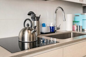 Ein Edelstahl-Wasserkocher auf einer modernen Induktionskochplatte, ein Küchenspülbecken und ein Wasserhahn.