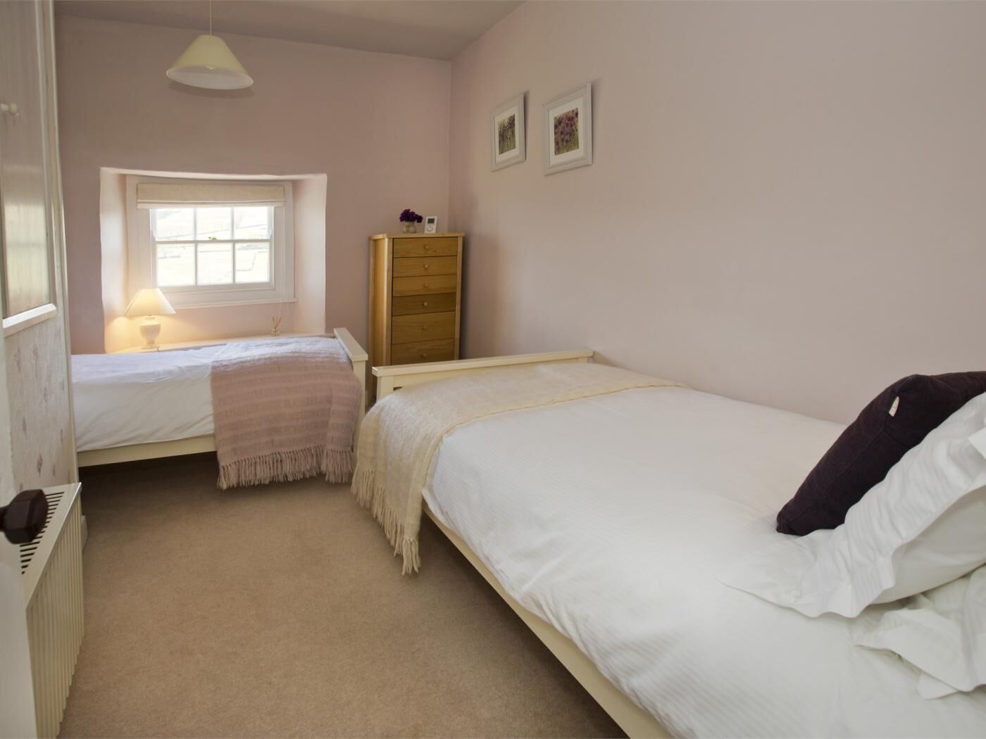 A bedroom with two beds, a window, a dresser, and a radiator.