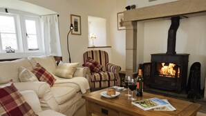 Ein gemütliches Wohnzimmer mit einer Couch, einem Sessel, einem Kamin und einem Tisch mit Teller, Weinglas und Zeitschrift.