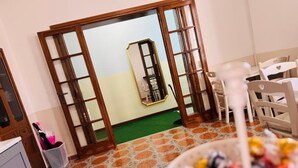 A room with a wooden-framed sliding door, a small seating area with a chair and table, and a bowl of fruit on the table. - Villa Matilde (Pisa)