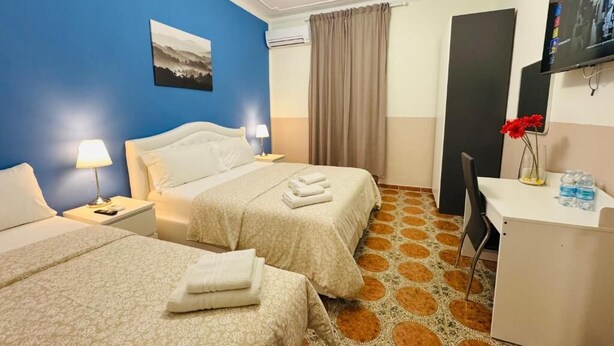 A hotel room with two beds, a desk, a chair, a TV, and a window with curtains. - Villa Matilde (Pisa)