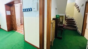 A hallway with green carpet, a wooden door, a staircase, and a medical cabinet. - Villa Matilde (Pisa)