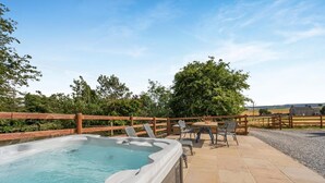 Un jacuzzi con cerramiento de madera, mobiliario exterior y vistas al campo.