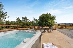 A hot tub with a wooden fence, outdoor seating, and a view of the countryside. - 2 Bed in Leyburn (oc-g0099) (Constable Burton)
