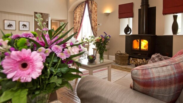 A cozy living room with a fireplace, a sofa, a coffee table, and a vase of flowers. - 1 Bed in Ripley (oc-g0127) (Kirkby Malzeard)