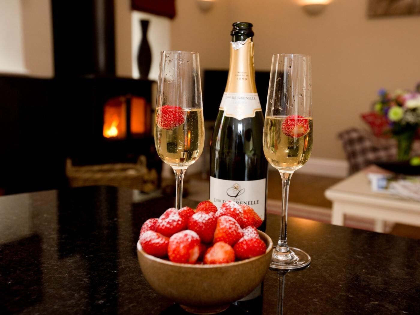 A bottle of champagne, two glasses, and a bowl of strawberries on a table.