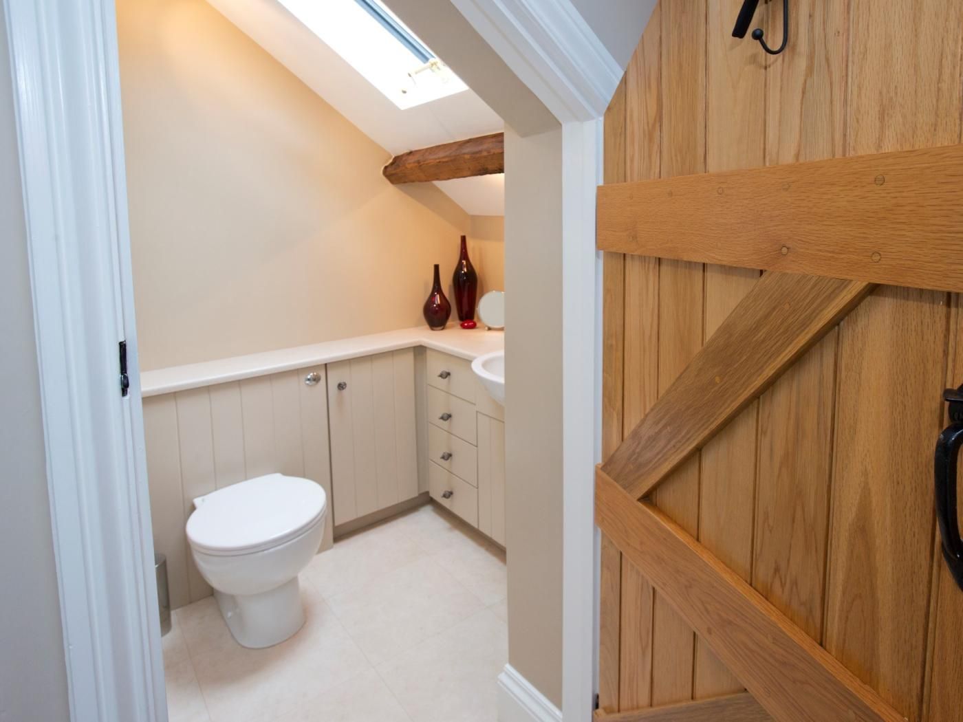 A compact bathroom with a white toilet, wooden cabinets, and a skylight.